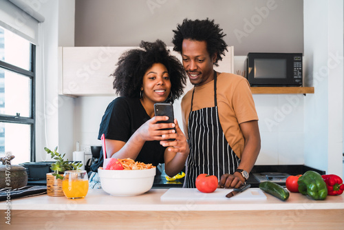 Wallpaper Mural Afro couple cooking together and using phone at home. Torontodigital.ca