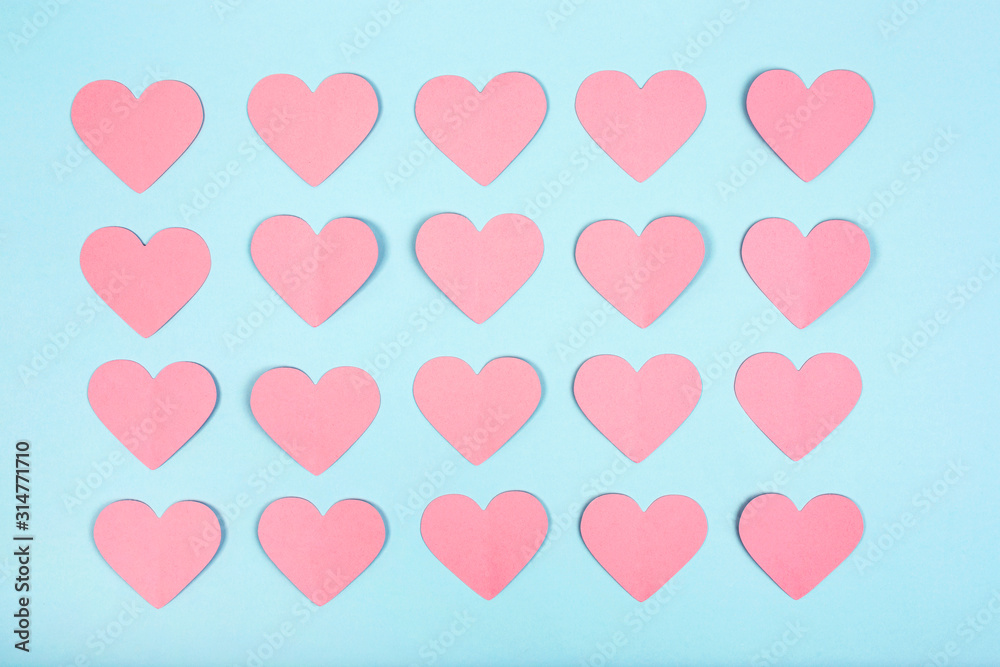 Pink paper hearts on blue background. Paper cut hearts arranged in rows on blue background. Flat lay