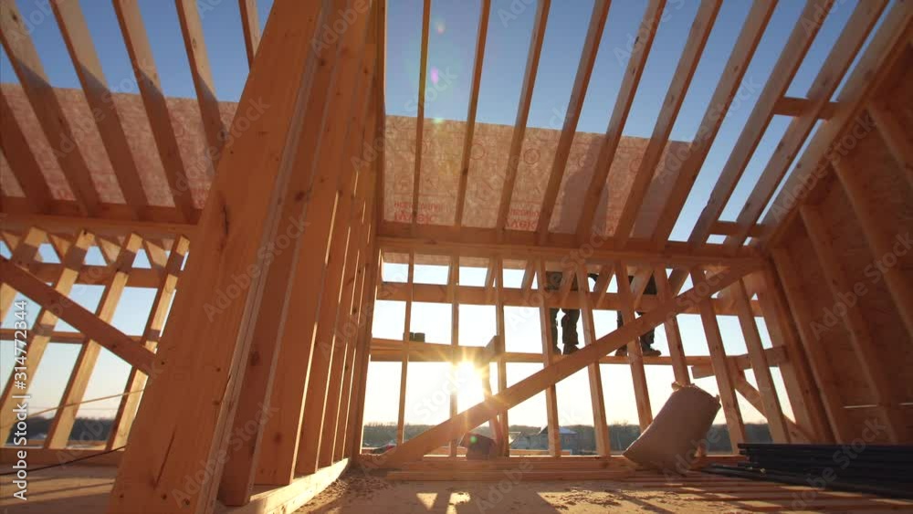 Sliding view from below of two builders covering roof with