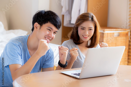 Beautiful portrait young asian couple working laptop with smile and happy sitting in bedroom, man and woman using notebook computer with excited and satisfied, business and success concept. © N_studio