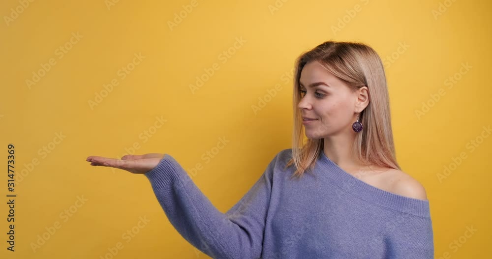 Slow motion portrait cheerful girl holding copy space palm on yellow background, looks turns her head to camera. Idea presentation your commercial product. Model advertises product. Ready advertising Slow motion portrait cheerful girl holding copy space palm on yellow background, looks turns her head to camera. Idea presentation your commercial product. Model advertises product. Ready advertising