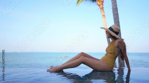 An attractive young sitting in the shallow edge of a resort infinity pool while she looks out to sea. photo