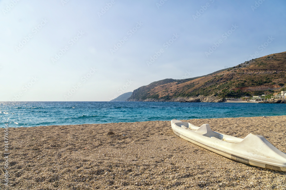 Active rest, sport, kayak. Single white kayak stand on a stony beach on the seashore of the Albanian Riviera.
