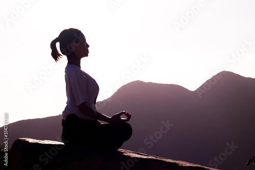 A young woman practices yoga at sunset  on a background of mountains and flowers.Girl performs asana Ardha padmasana lotus position  meditates with panoramic view. Copy Space