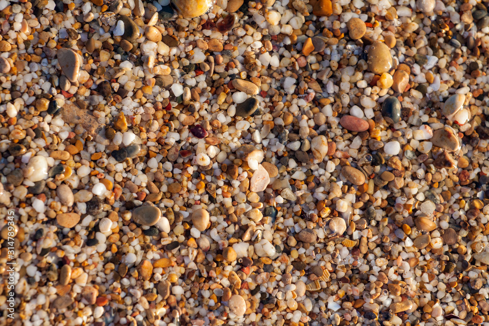 sea pebbles colored granite on the beach background stones. The shore of the beach with sand and pebbles washed by the waves of the sea.