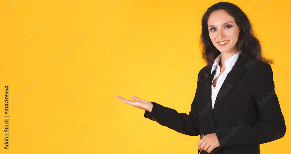 Portrait of a beautiful Caucasian young businesswoman smiling looking at the camera, presenting with hand open to copy space empty. Studio shot isolated on yellow background banner. Portrait of a beautiful Caucasian young businesswoman smiling looking at the camera, presenting with hand open to copy space empty. Studio shot isolated on yellow background banner.