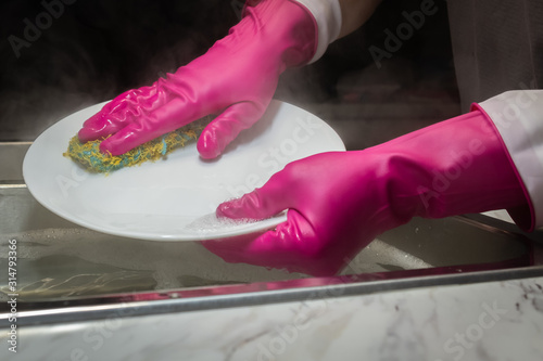 Fotografía Close up of a model's hands washing dishes in steaming hot water with hot pink or salmon colored rubber gloves with anit-drip cuffs