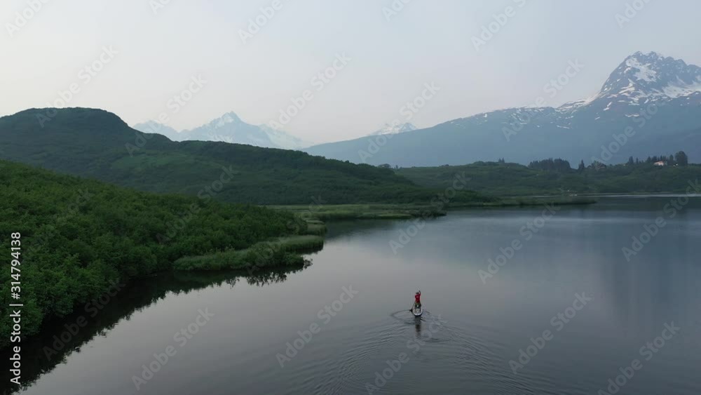 Drone flyover of paddle boarder along green shoreline of bushes Drone flyover of paddle boarder along green shoreline of bushes