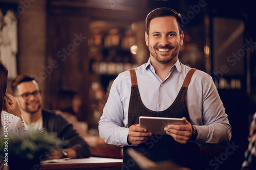 Portrait of happy waiter with digital tablet in a bar.