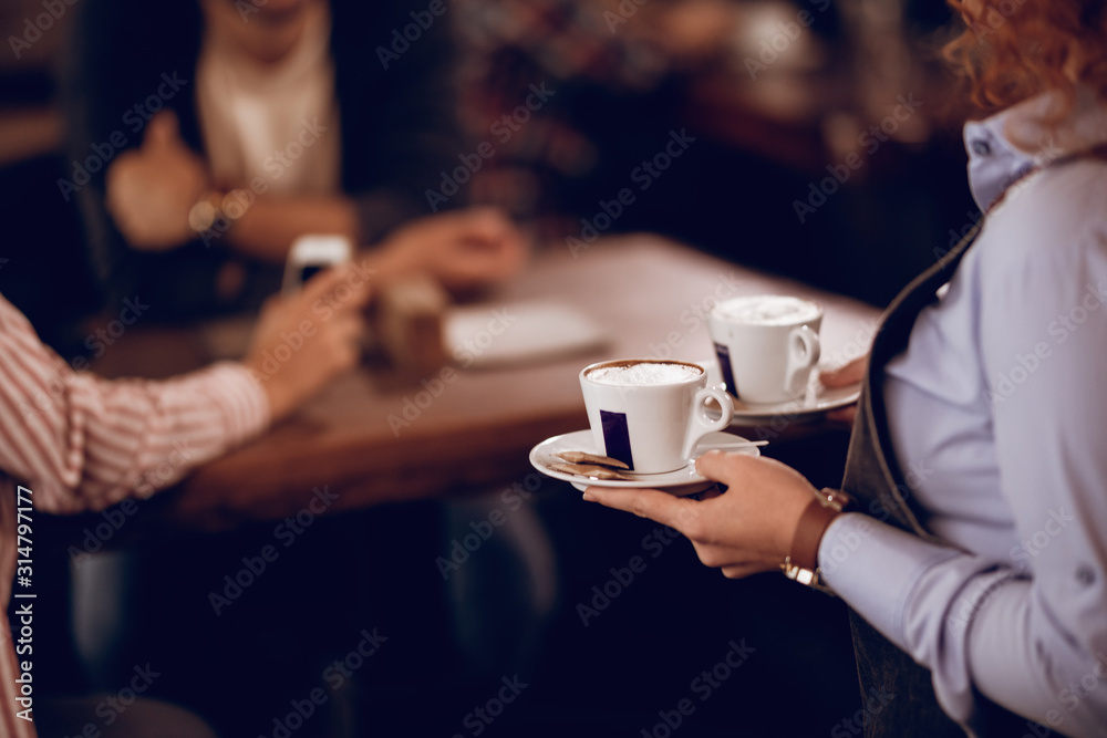 Close-up of waitress bringing coffee to guests in a cafe.