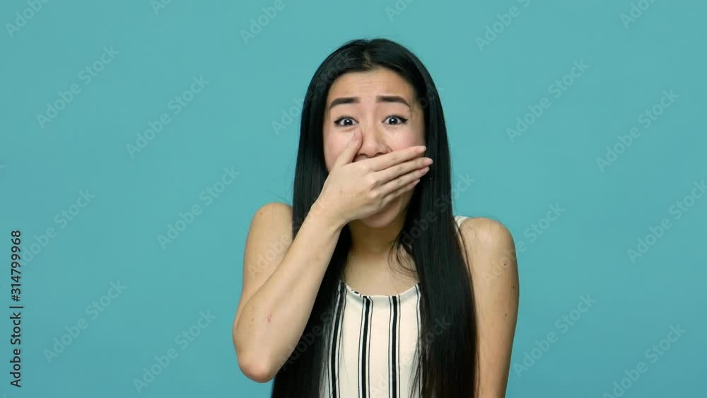 I won't say anyone! Intimidated asian woman with long hair screaming of fear and covering mouth with hand, scared to tell truth, terrified to speak. indoor studio shot isolated on blue background I won't say anyone! Intimidated asian woman with long hair screaming of fear and covering mouth with hand, scared to tell truth, terrified to speak. indoor studio shot isolated on blue background