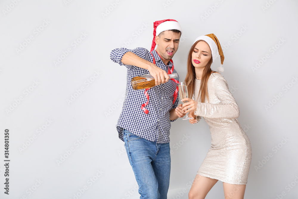 Fototapeta premium Drunk couple celebrating New Year against light background