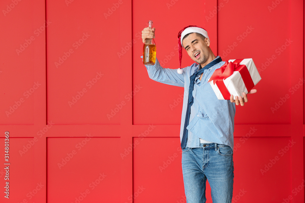 Drunk man with Santa Claus hat, gift and champagne on color background