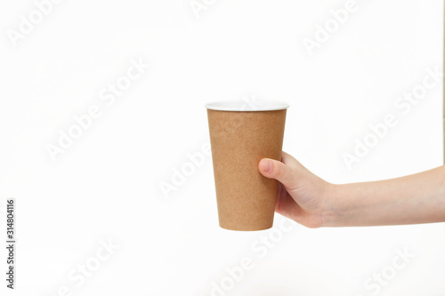 Eco kraft paper tableware. Children's hand holds a paper disposable cup isolated on white background. Recycling concept. Zero waste.