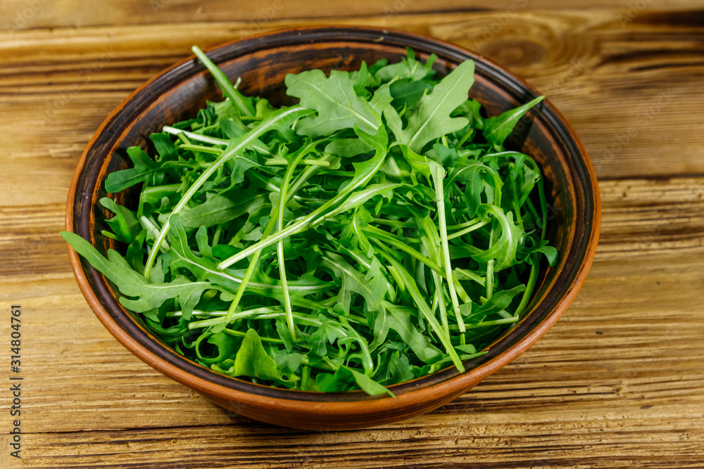 Fresh green arugula in ceramic bowl on a wooden table. Healthy food or vegetarian concept Fresh green arugula in ceramic bowl on a wooden table. Healthy food or vegetarian concept