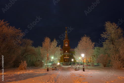The building of the Orthodox Church at night surrounded by trees in the snow.