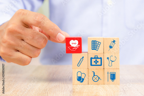 Close-up hand choose wooden toy blocks with medical equipment bag icon for health insurance concepts.