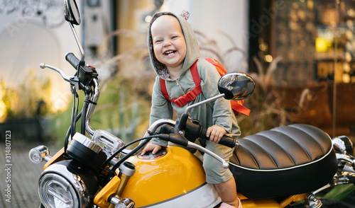 Small happy baby in a bodysuit sits on a motorcycle and experiences an emotion of joy. Motorcycle advertising.