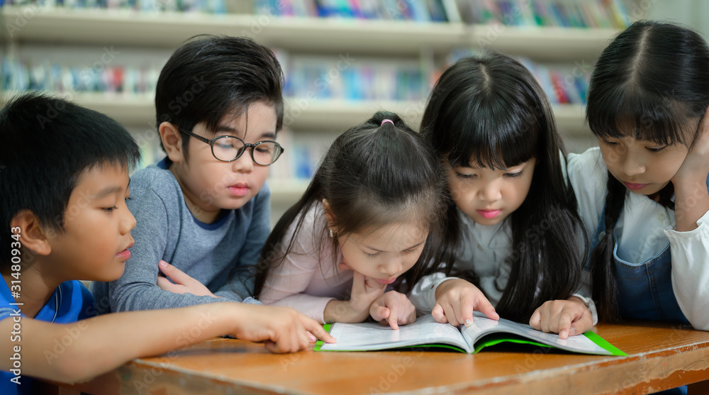 A Group of Asian Kids Reading Book in School Library with a Shelf of Book in Background, Asian Kid Education Concept A Group of Asian Kids Reading Book in School Library with a Shelf of Book in Background, Asian Kid Education Concept