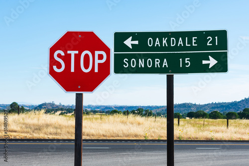 An 8-sided red STOP sign and rectangular shaped green guide road sign with white lettering. Direction and distance to Oakdale and Sonora. Background California's iconic golden grass and landscape