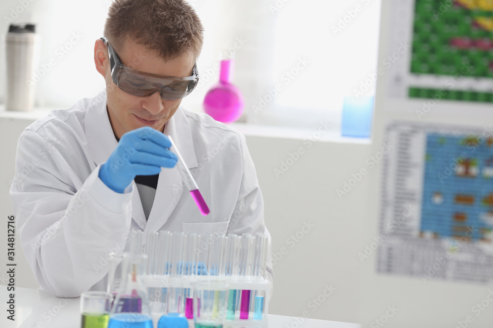 Fototapeta premium A male chemist holds test tube of glass in his hand overflows a liquid solution of potassium permanganate conducts an analysis reaction takes various versions of reagents using chemical manufacturing.