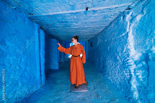 a tourist in a bright orange dress to the heels walks along the long corridor of the blue city of Morocco © nelen.ru
