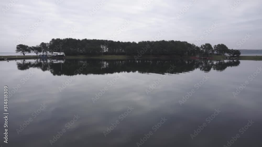 Tilt up shot of lake and reflection of forest island in the water Tilt up shot of lake and reflection of forest island in the water