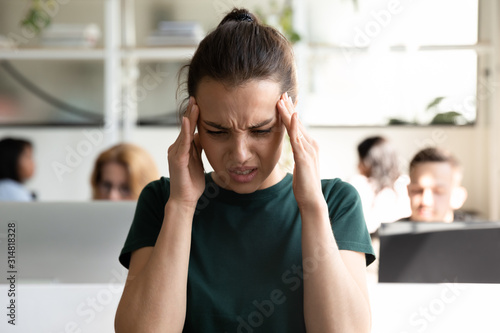 Foto Female office worker suffers from sudden throbbing headache