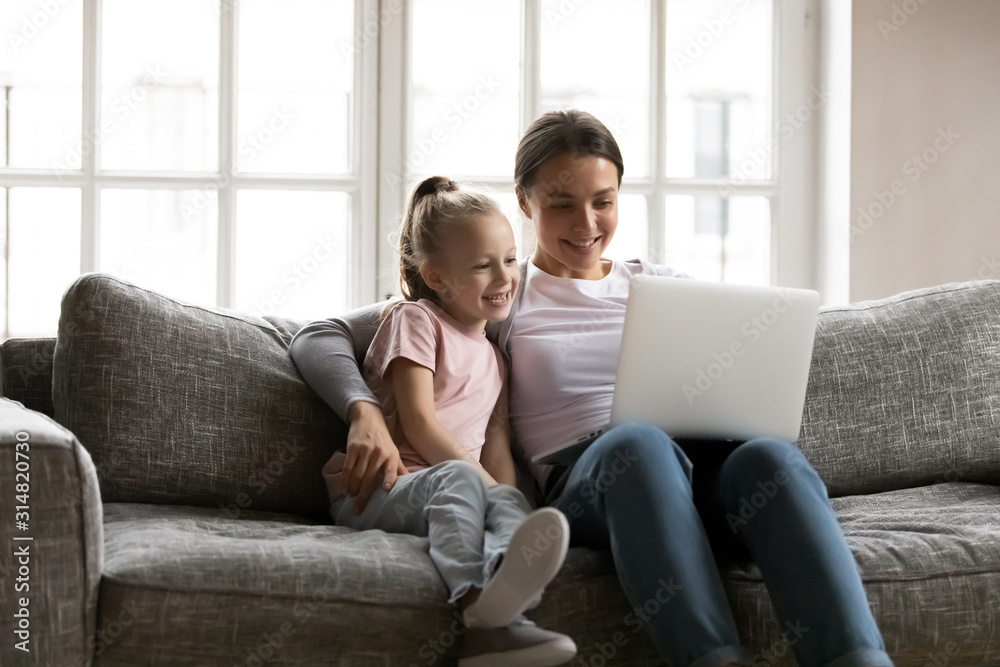 Happy mum and small daughter watch video on laptop Happy mum and small daughter watch video on laptop
