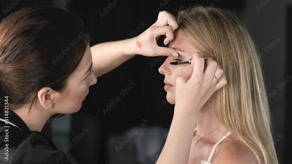 An artist is doing a makeup. A client is a young lady. The girls are in a salon. An artist is doing a makeup. A client is a young lady. The girls are in a salon.