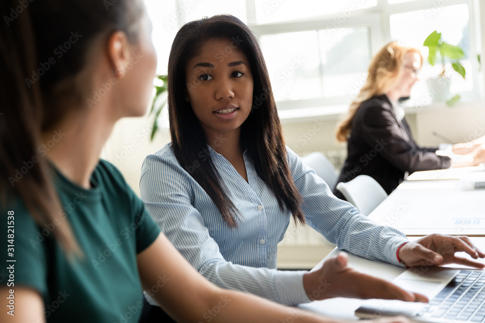 African office worker helps to apprentice sitting at shared desk African office worker helps to apprentice sitting at shared desk