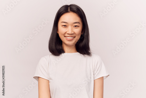 Portrait of beautiful smiling young woman grins at camera, grinning, eyes glistening. Businesslike young woman Asian appearance with black hair brown eyes stands isolated white background in Studio