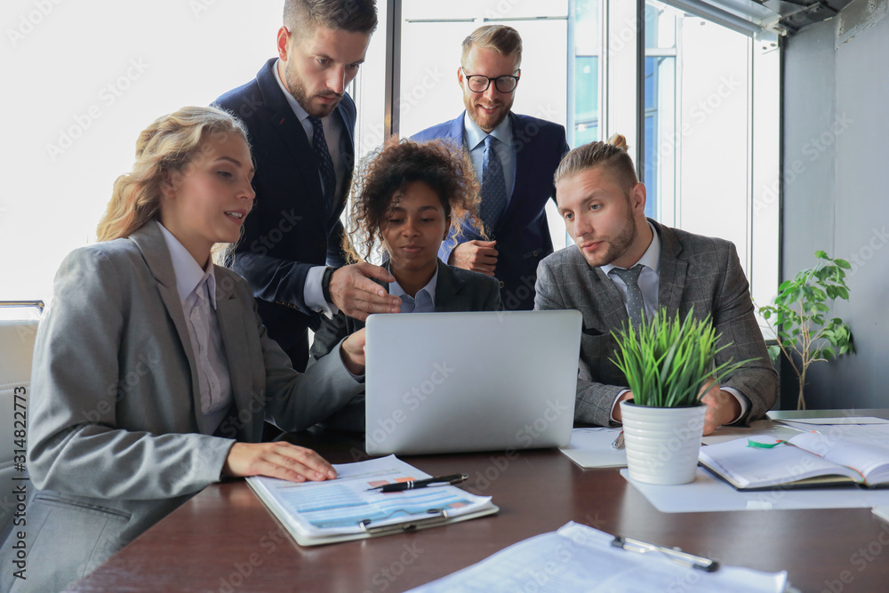 Group of young modern people in formalwear smiling and discussing something while working in the modern office Group of young modern people in formalwear smiling and discussing something while working in the modern office