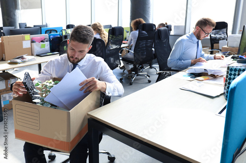 Sad dismissed worker are taking his office supplies with him from office photo