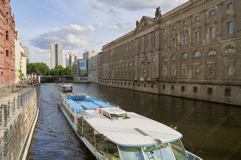 Tourist ship sails along the Shree river. Horizontal photo of colorful clean European city of Berlin in Germany, daytime, cloudy sky, month of may, travel in tourist place.