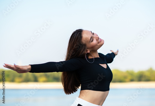 Charming brunette girl smiling and enjoying life outdoor. Young woman, summer portrait. Female model posing over nature background with river, beach and blue clean sky. Freedom, youth lifestyle
