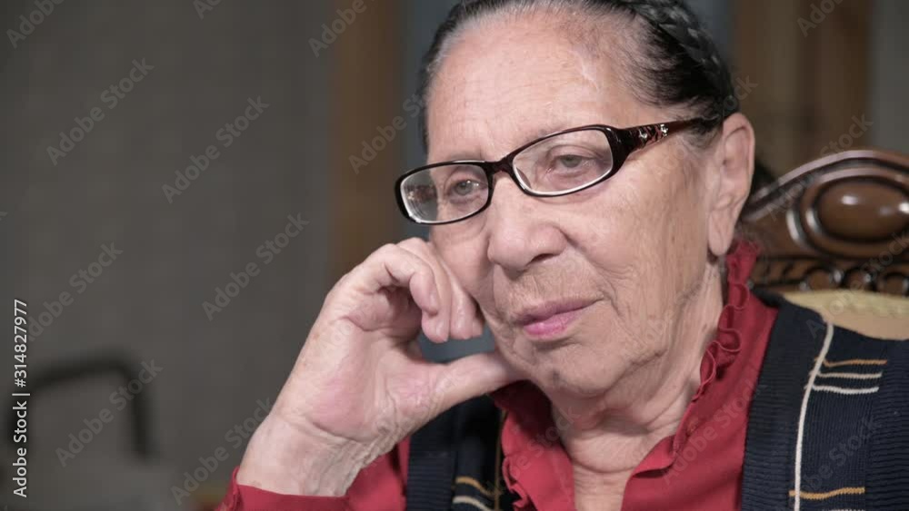 Portrait of an elderly pensive woman in glasses leaning on her arm indoors sitting and thinking. Elderly woman 80 years old Portrait of an elderly pensive woman in glasses leaning on her arm indoors sitting and thinking. Elderly woman 80 years old