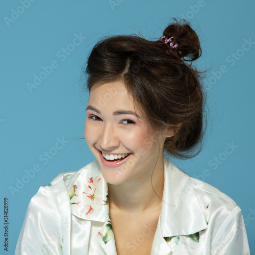 Cheerful attractive sleepy teen girl wearing pyjamas looking at camera like at mirror in the morning, isolated over blue background. Young pretty woman in early before morning procedures. photo