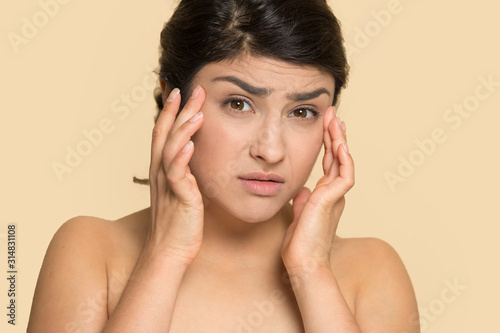 Frowning young indian ethnicity woman examining wrinkles.