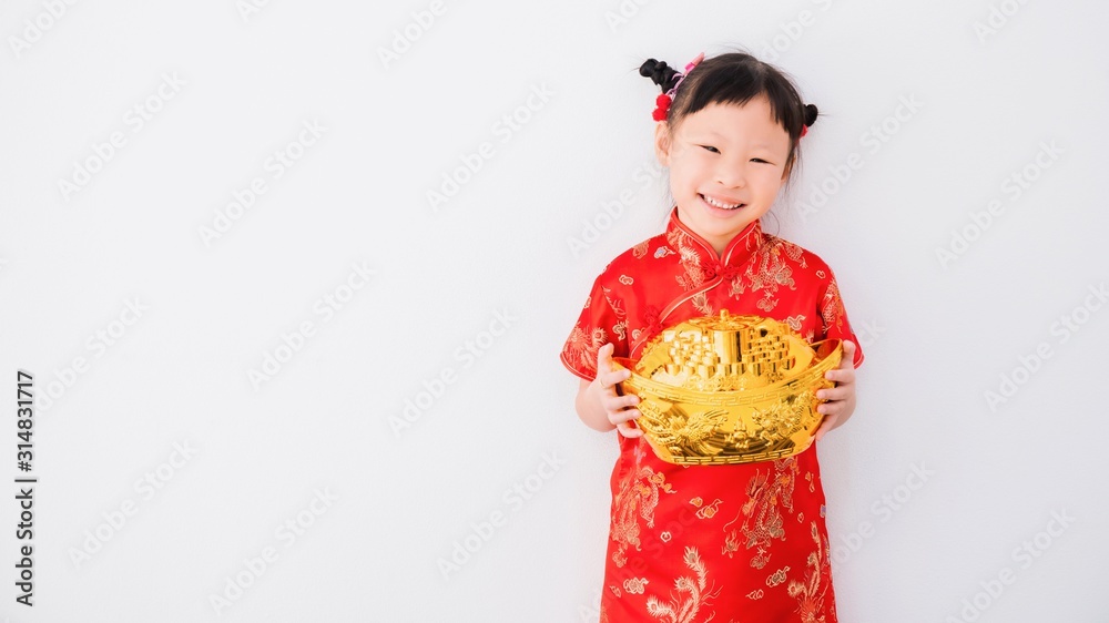 Smiling little Asian girl in chinese traditional dress holding Chinese gold money on white wall background with copy space.Happy chinese new year concept. Smiling little Asian girl in chinese traditional dress holding Chinese gold money on white wall background with copy space.Happy chinese new year concept.