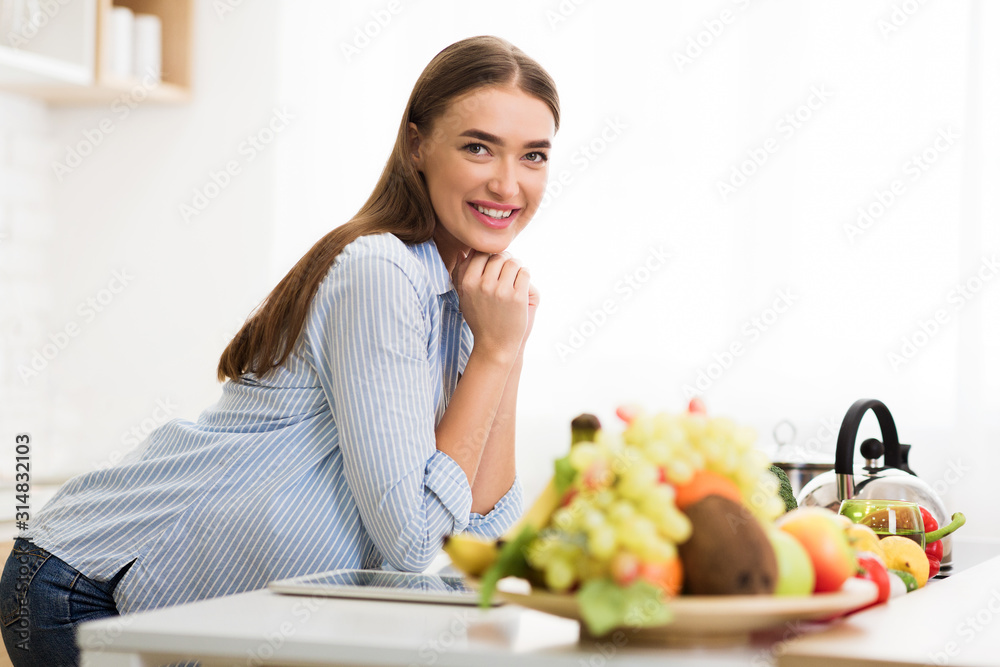 Woman posing in kitchen near table with fresh fruits
