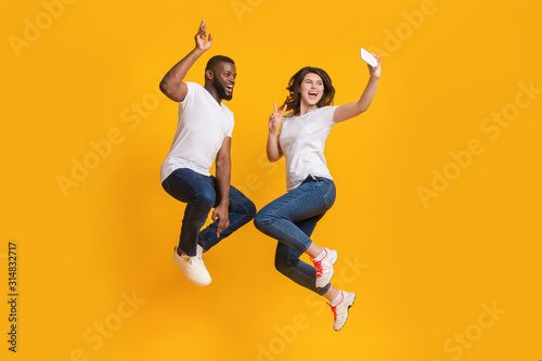 Cheerful Interracial Couple Taking Selfie While Jumping In Air