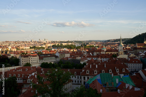 Typical roofs. Top view - roofs with red tiles in old buildings. There are beautiful houses in green trees. Horizontal photo colorful European city Prague in Czech Republic, travel in tourist place © EverGrump