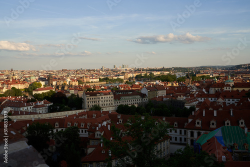 Typical roofs. Top view - roofs with red tiles in old buildings. There are beautiful houses in green trees. Horizontal photo colorful European city Prague in Czech Republic, travel in tourist place