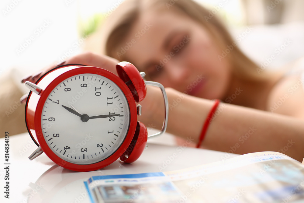 A young woman can not wake up at 7 am to work after a tumultuous party under the alarm clock - obrazy, fototapety, plakaty 