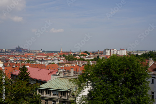 Typical roofs. Top view - roofs with red tiles in old buildings. There are beautiful houses in green trees. Horizontal photo colorful European city Prague in Czech Republic, travel in tourist place