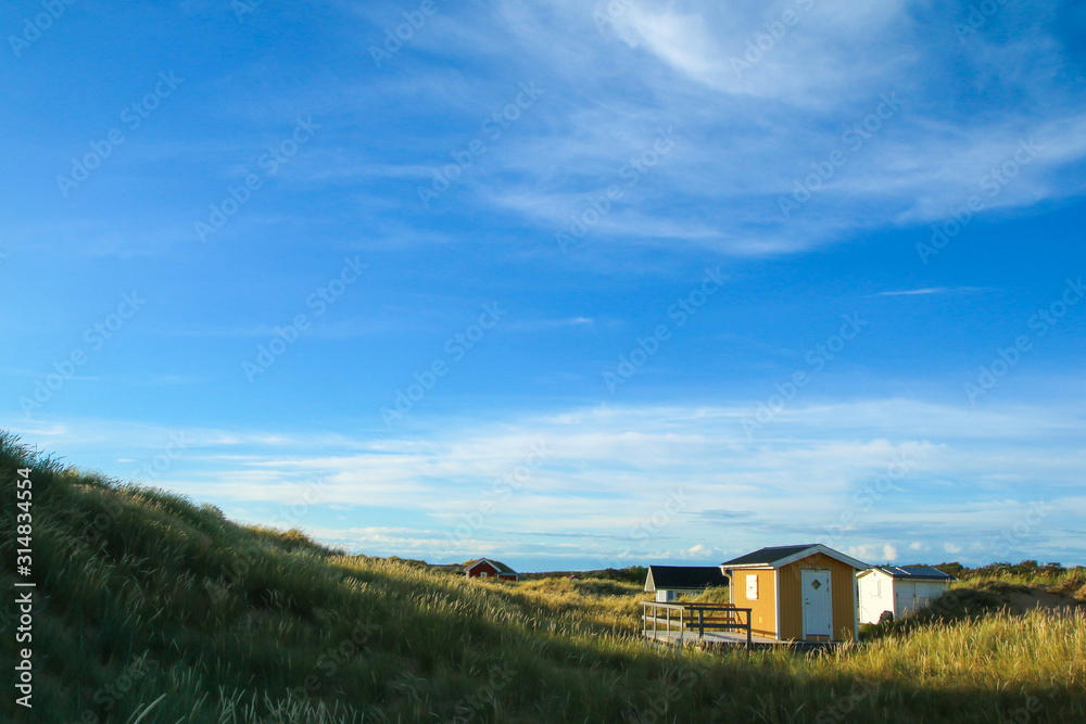 The traditional colorful wooden recreational cottages by the coast of the sea in Sweden, hidden behind the dunes.