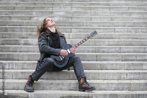 Rock guitarist on the steps. A musician with a bass guitar in a leather suit. Metalist with a guitar on the background of industrial steps. photo