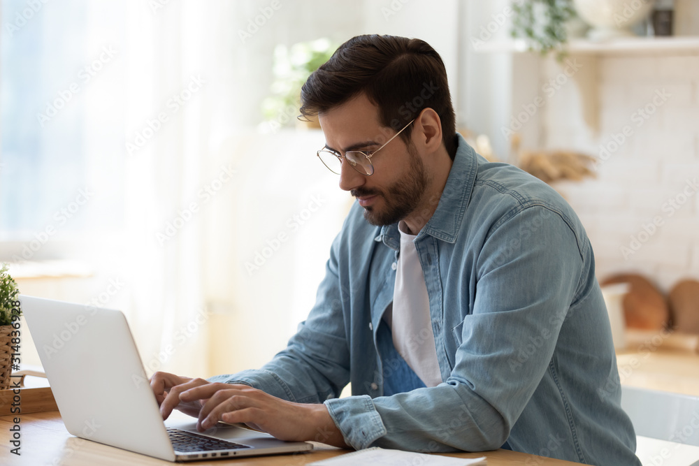 Handsome young businessman in eyewear working with computer remotely.