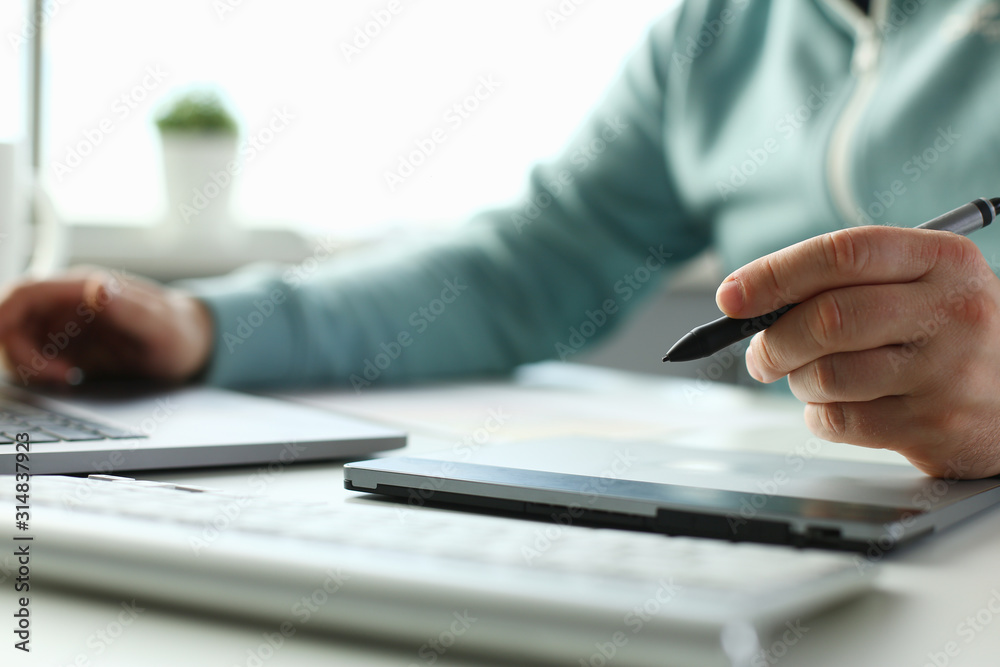A young designer holds pen from tablet in hand working on new project for customer in field of building construction projects. A young designer holds pen from tablet in hand working on new project for customer in field of building construction projects.